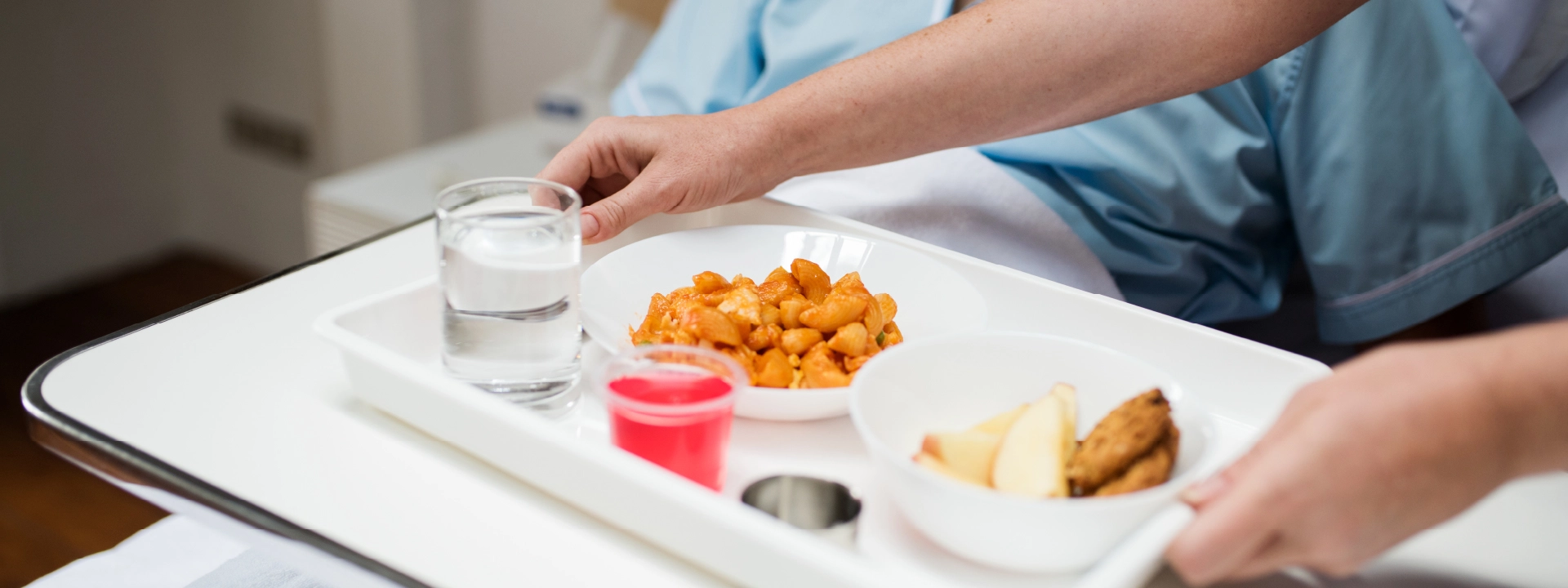 Eine Pflegekraft reicht einem Patienten ein Tablett mit Essen ans Bett. 