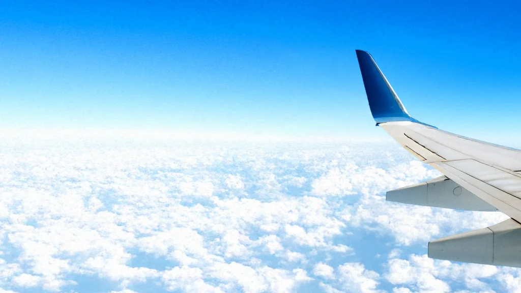 Symbolbild durchstarten für DRG Forum 2025: ein Flugzeug über den Wolken, nur die linke Tragfläche vor blauem Himmel ist sichtbar
