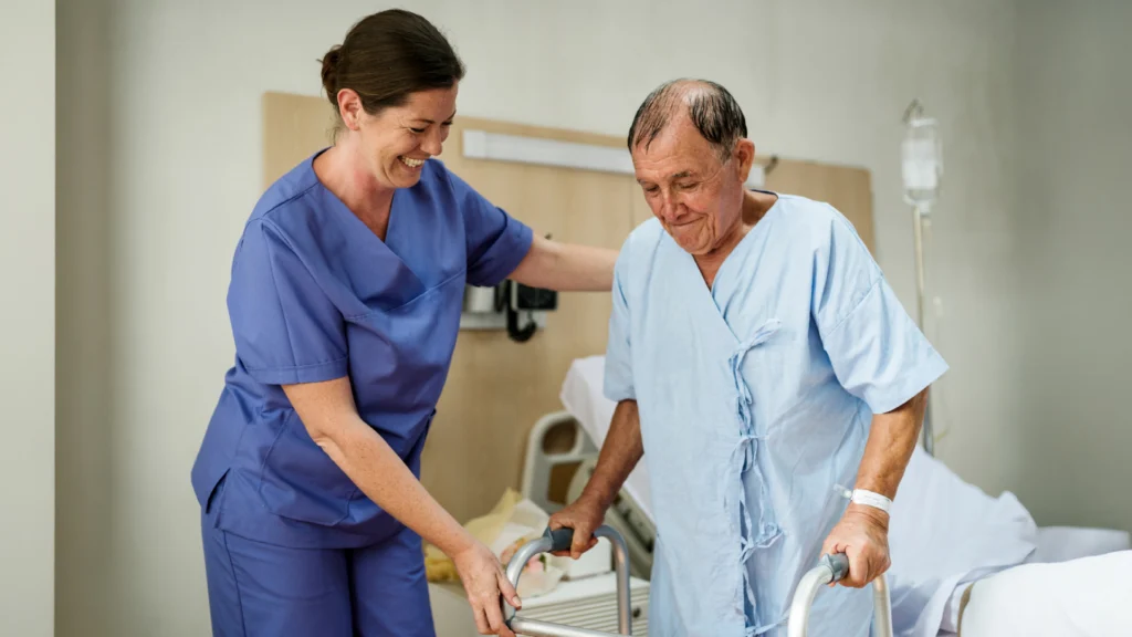 Eine Pflegerin in einem Krankenhaus hilft einem Patienten beim Aufstehen.